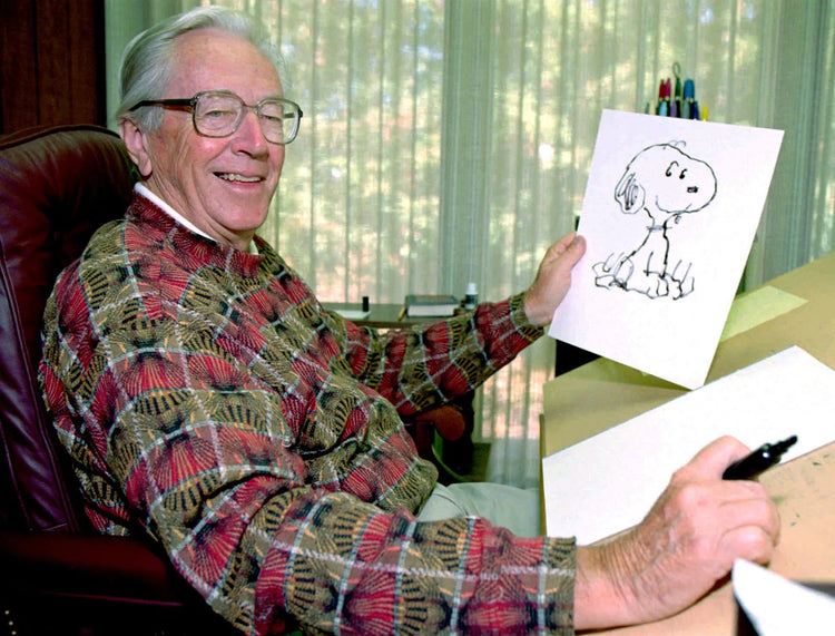 Charles schulz sitting on chair displaying drawing of Snoopy Boston memorabilia